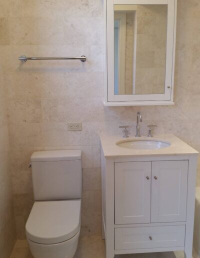 A modern bathroom with beige tiles featuring a white toilet, sink vanity, and a mirrored medicine cabinet.