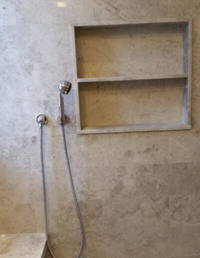 A modern bathroom shower area with a handheld shower head and built-in wall shelf.
