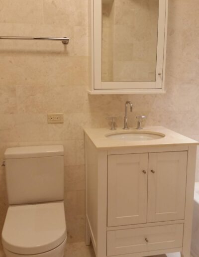 A modern bathroom interior featuring a white toilet and a white vanity cabinet with a built-in sink and a mirror above it.