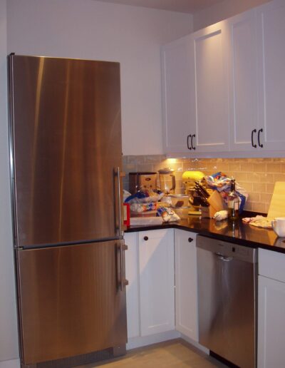 Modern kitchen with stainless steel refrigerator and white cabinets.