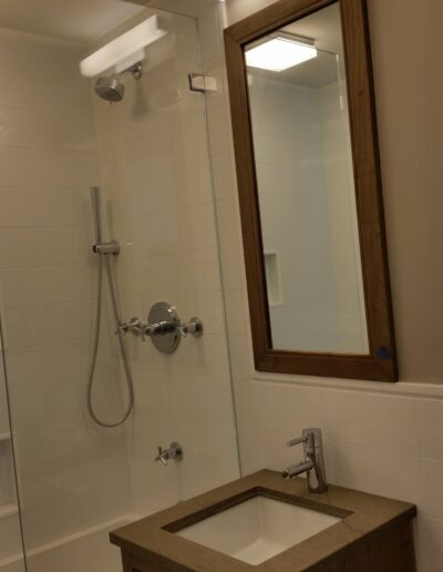 A modern bathroom interior featuring a glass shower enclosure, a wall-mounted mirror, and a wooden vanity with a built-in sink.